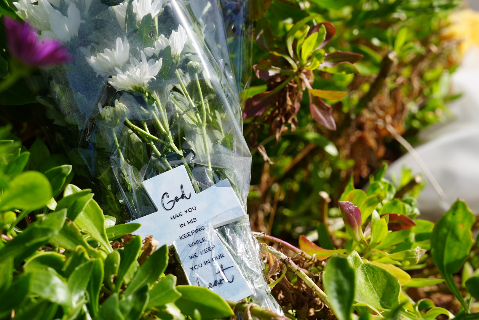 Flowers with a card written saying 'God has you in his keeping while we keep you in our heart'