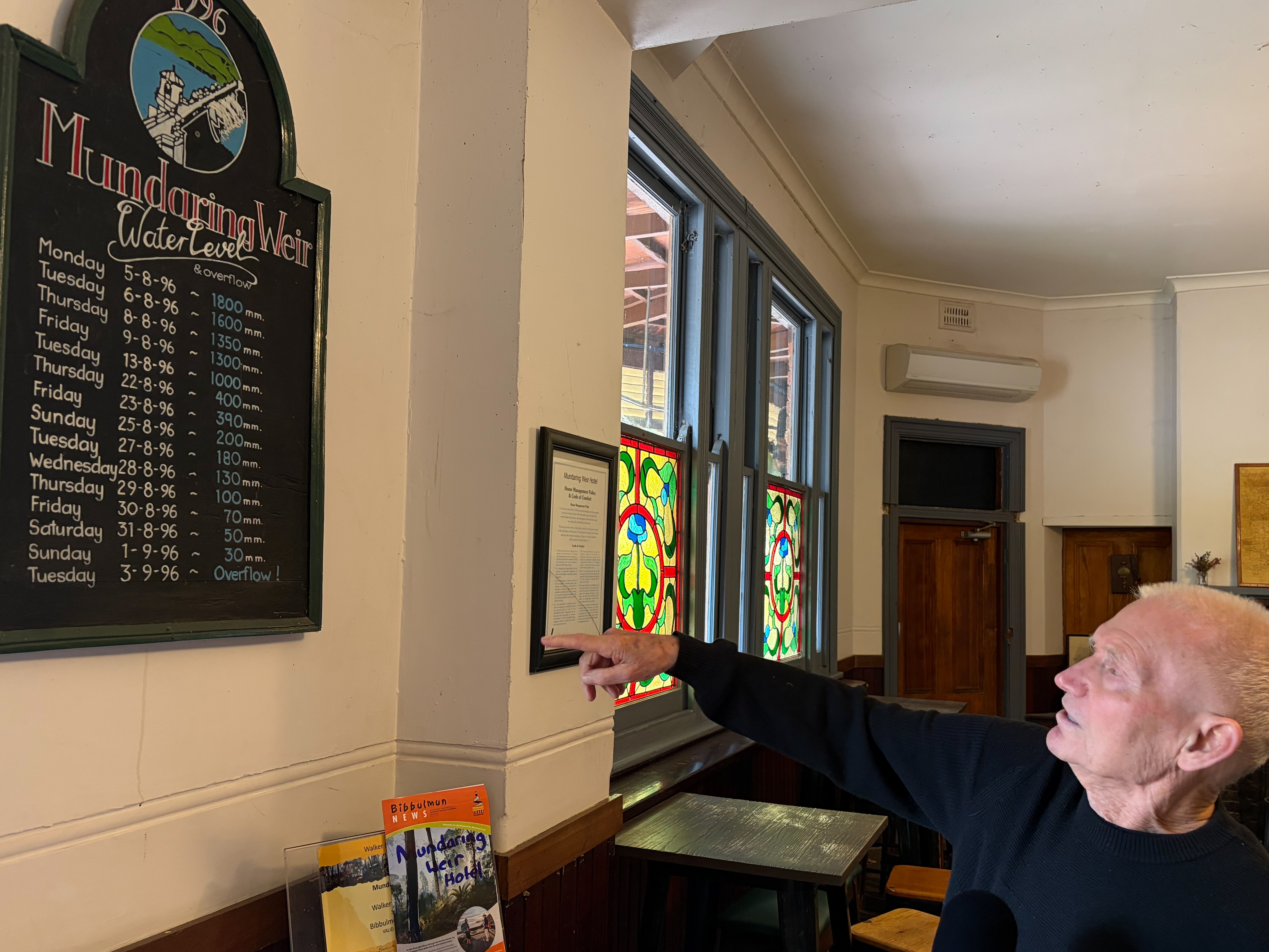Old man pointing at hand painted board in bar