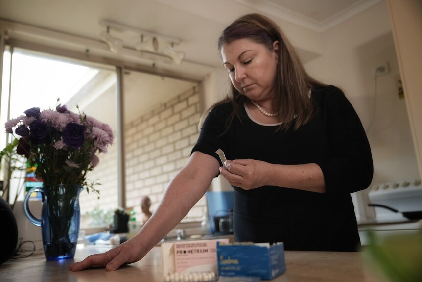 Caroline Deane stands in her kitchen with medication on the kitchen bench.