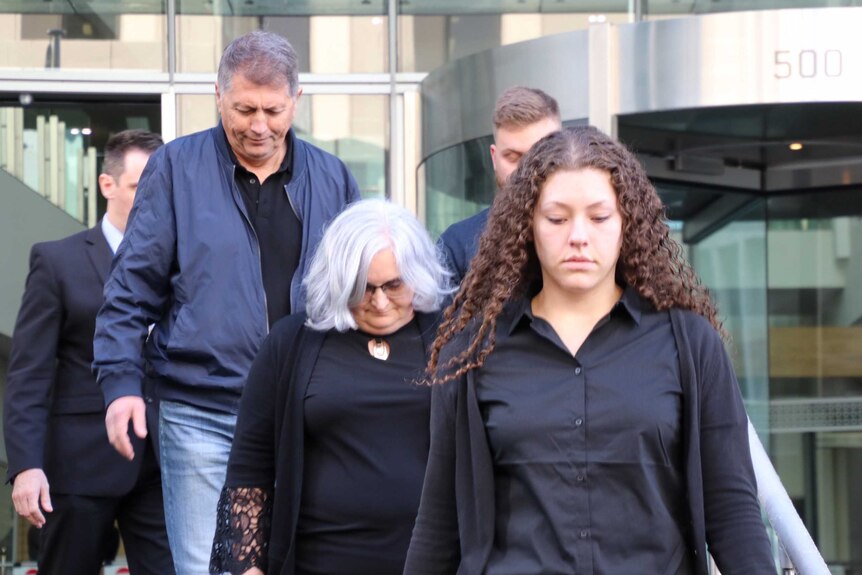 A younger and an older woman walk out of the Perth District Court in Perth with their heads down and with a man behind them.
