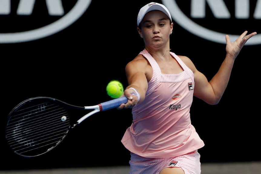 A woman wearing a pink singlet looks at the ball as her racquet approaches the ball, being held in one hand.