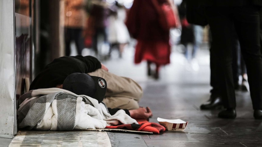 Homeless man sleeping on the footpath in Elizabeth Street in Melbourne's CBD as pedestrians walk past