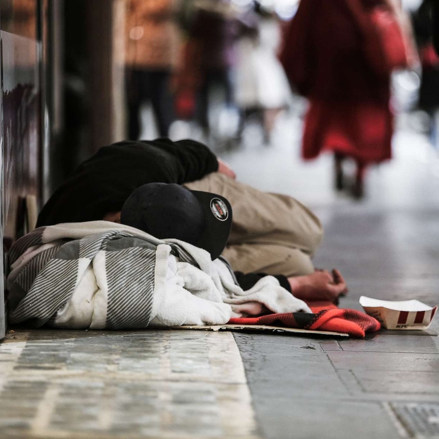 Homeless man sleeping on the footpath in Elizabeth Street in Melbourne's CBD as pedestrians walk past