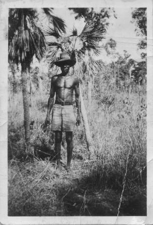 monochrome of man standing in the bush wearing shorts and a hat.