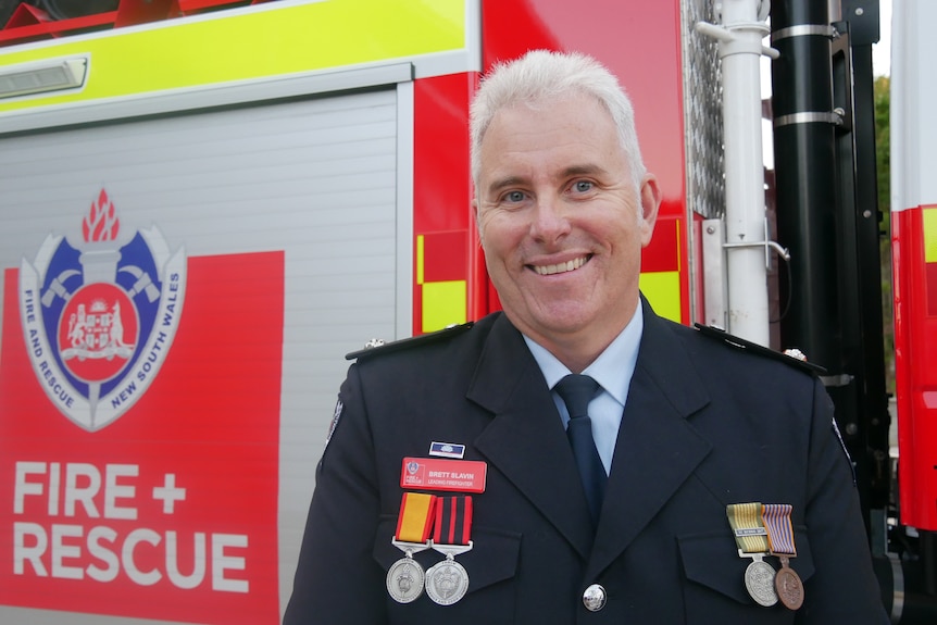 Man in suit with firefighting medals stands in front of fire truck 