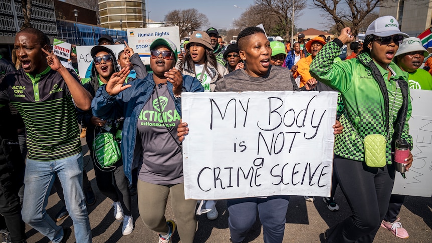 Protestors, some wearing green, walk together shouting, wearing a sign that says 'my body is not a crime scene'.