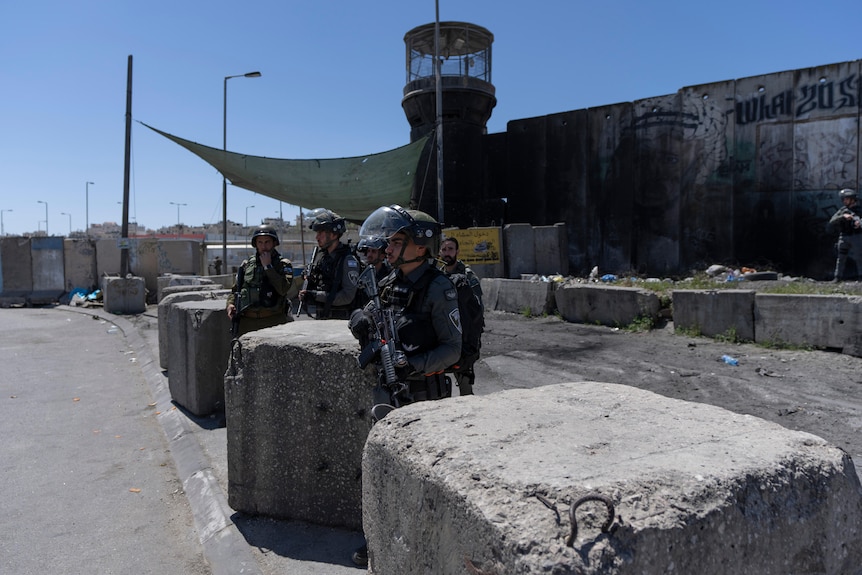 People in helmets and holding guns in front of stone blocks.
