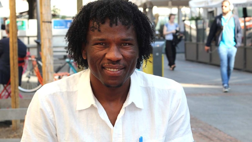 A Sudanese refugee sits at a cafe in Geneva, half-smiling.