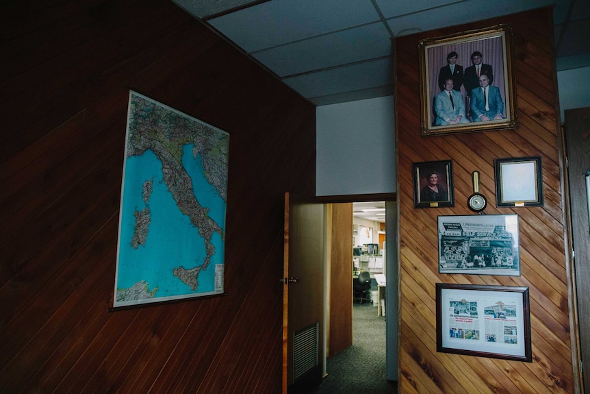 The wood panelled office wall, covered of pictures of family and an Italian map