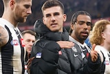 An injured Nick Daicos is wearing a Collingwood puffer jacket as he walks off the field with his teammates