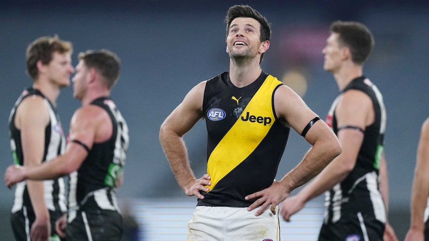 An AFL player smiles ruefully and looks to the sky after his team draws a match.