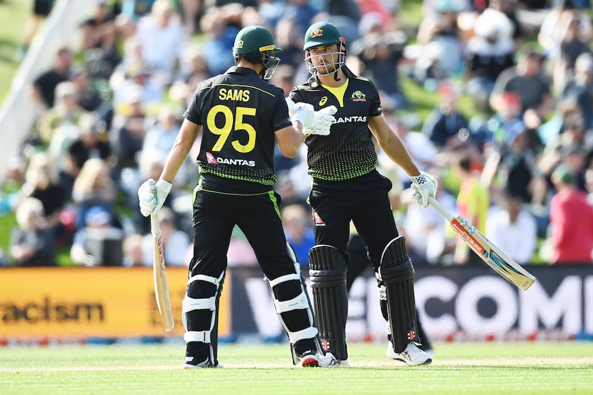 Two international cricketers meet mid-pitch and touch gloves during a big T20I partnership.