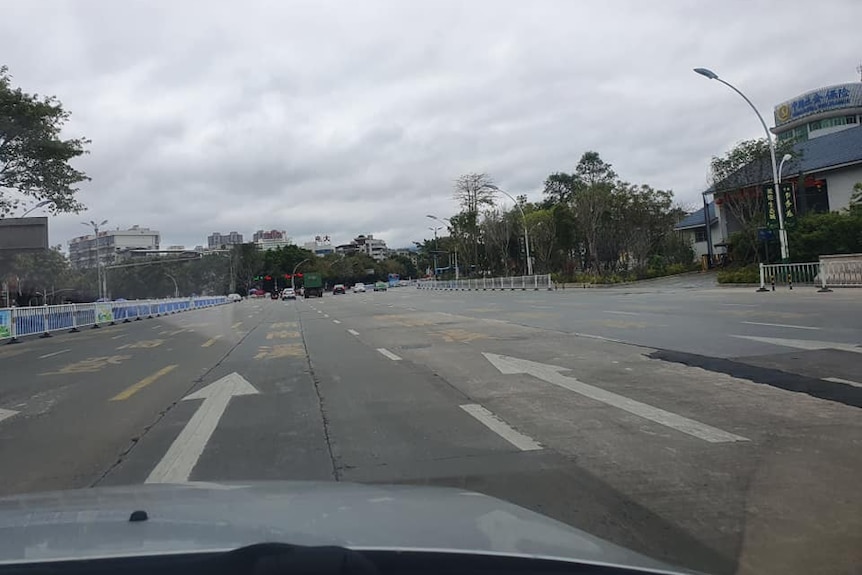 A car is driving down an empty street. There are Chinese signs in the background.