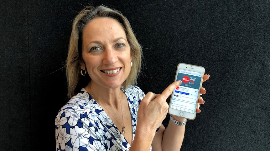 A smiling woman holding a phone pointing to a Facebook page