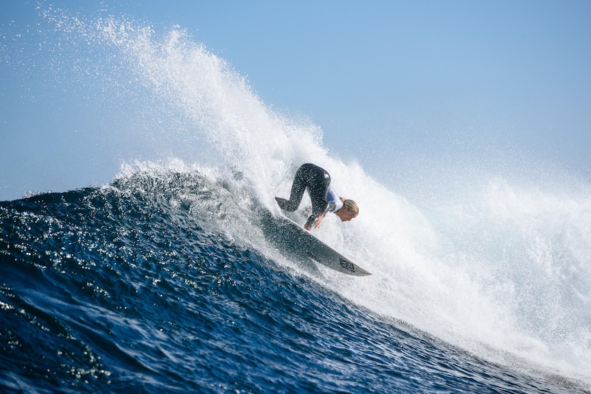 A woman mid-wave surfing on a clear blue sky day