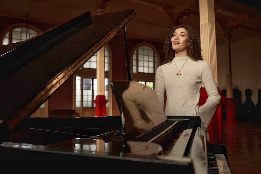 A woman is standing singing next to a grand piano which has its lid lifted up.