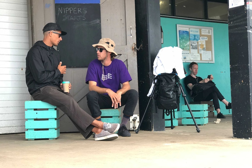 Soli Bailey, sitting on a milk crate and holding a coffee, chats to a man. Both look very surfy, you'd have to say.