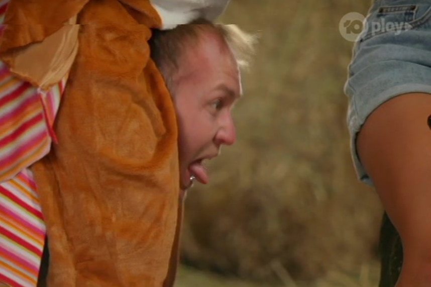 A man in a horse costume sticking his tongue out near a woman's leg.
