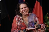 Leanne Liddle stands and smiles holding her NT Australian of the Year award.