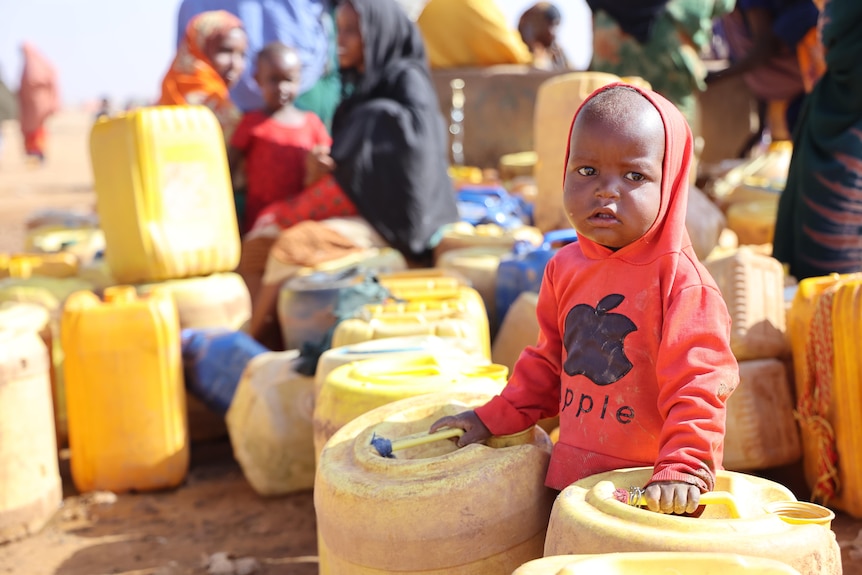 A boy stands amid water jugs.
