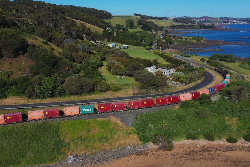 An aerial view of a train snaking its way along a green rural coastline.