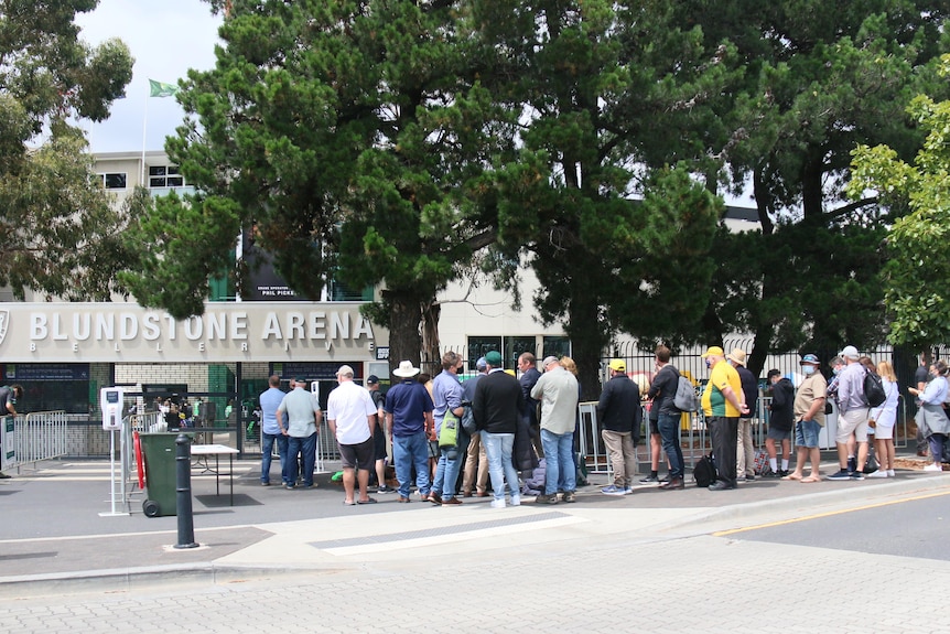 Dozens of people in a queue outside a sport stadium.
