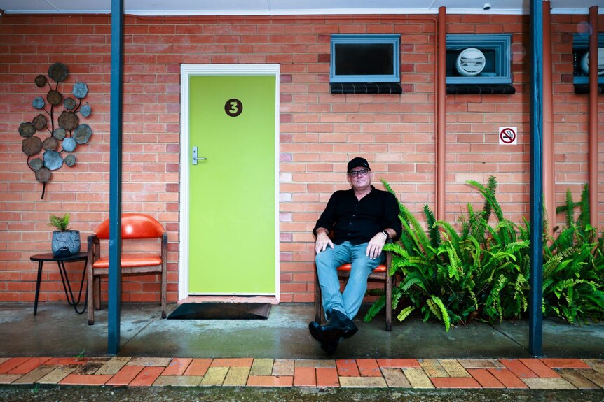 Richard Stanwix sits outside his Warburton motel with a bright green door behind him