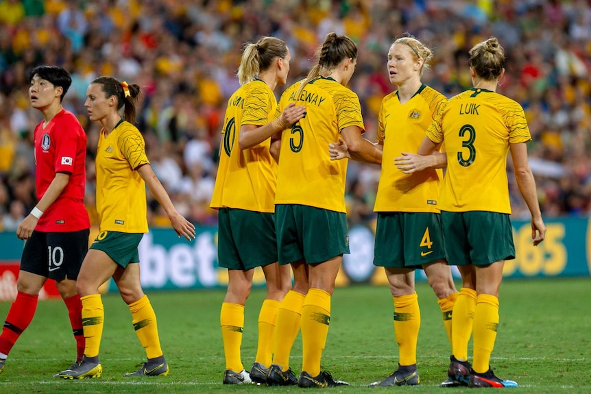 Clare Polkinghorne faces the opposite way to her three teammates, who stand in a line with their arms linked.