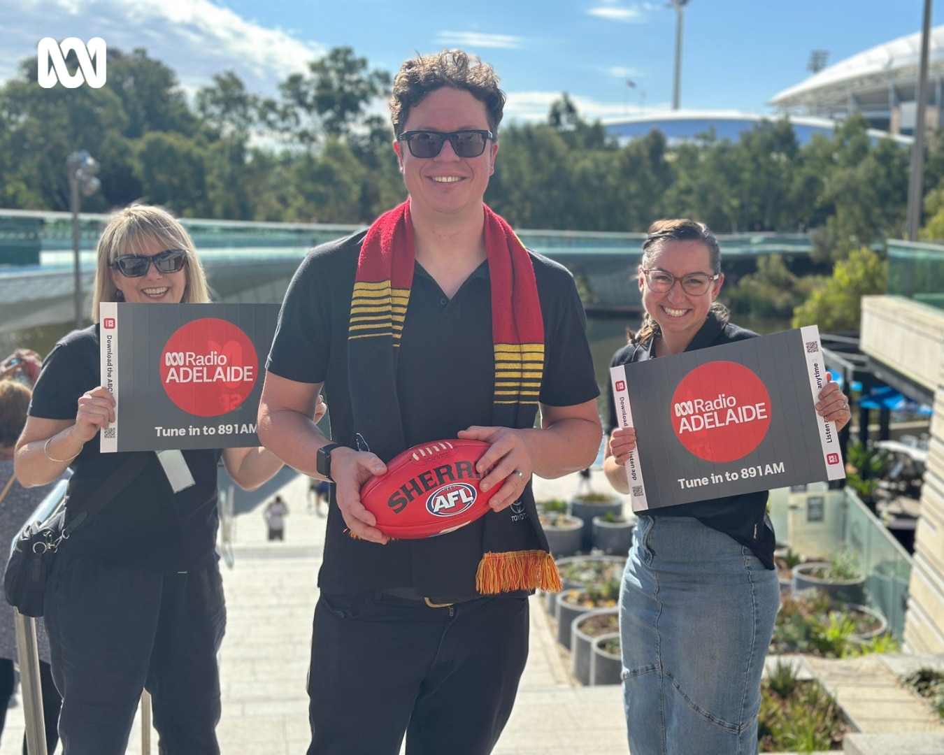 group of people holding ABC Radio Adelaide cards and football