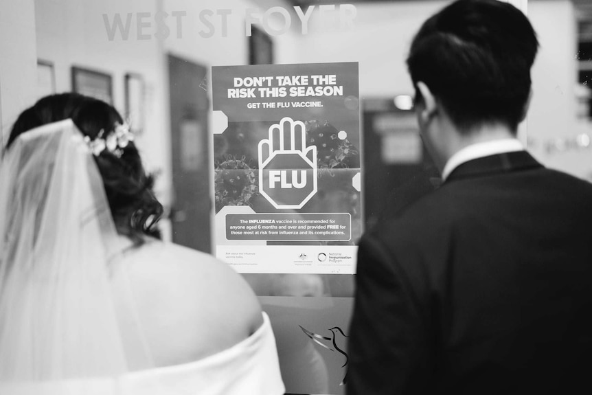 A bride and groom in front of a COVID-19 health warning sign