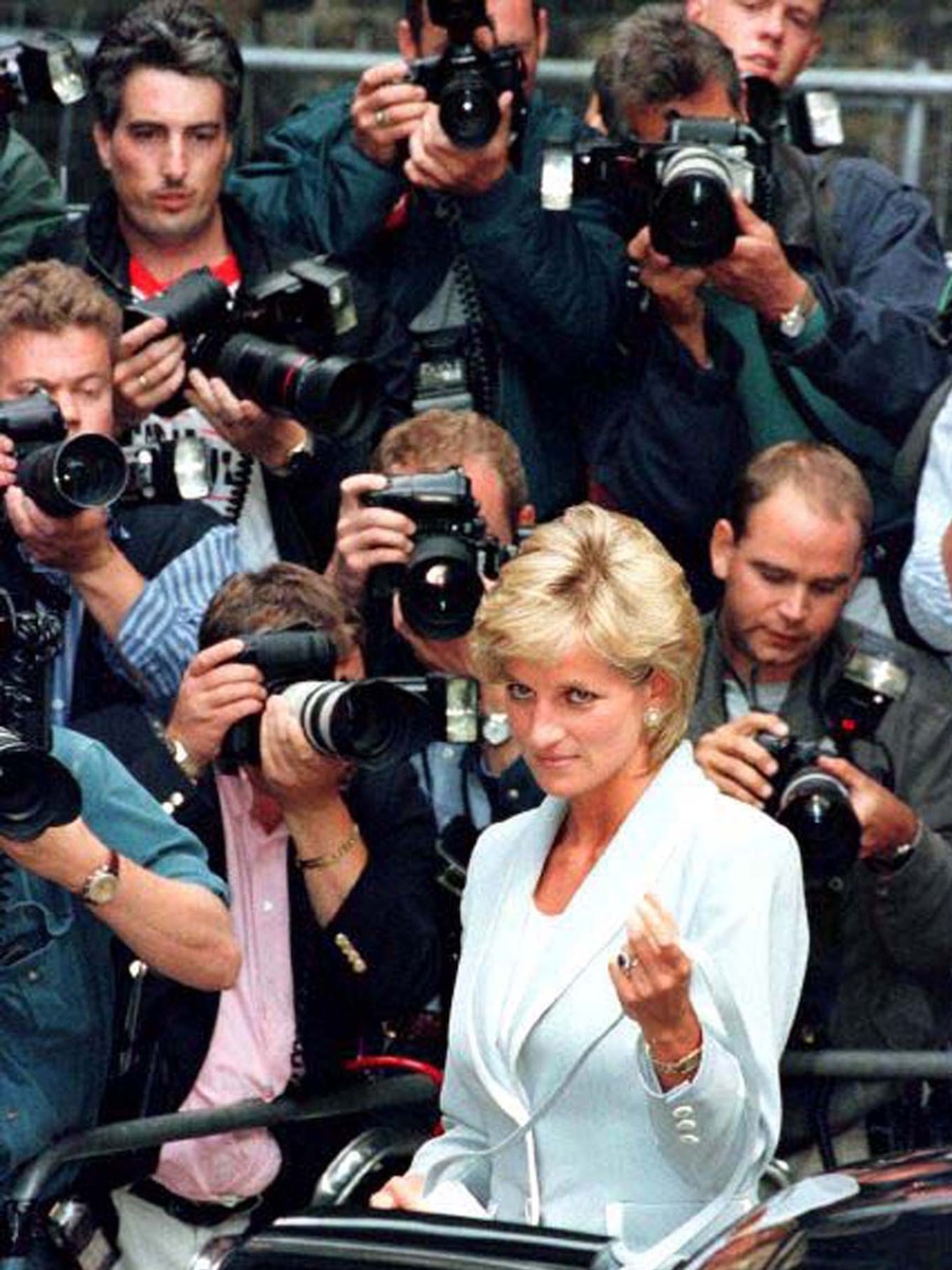 A blonde woman surrounded by photographers