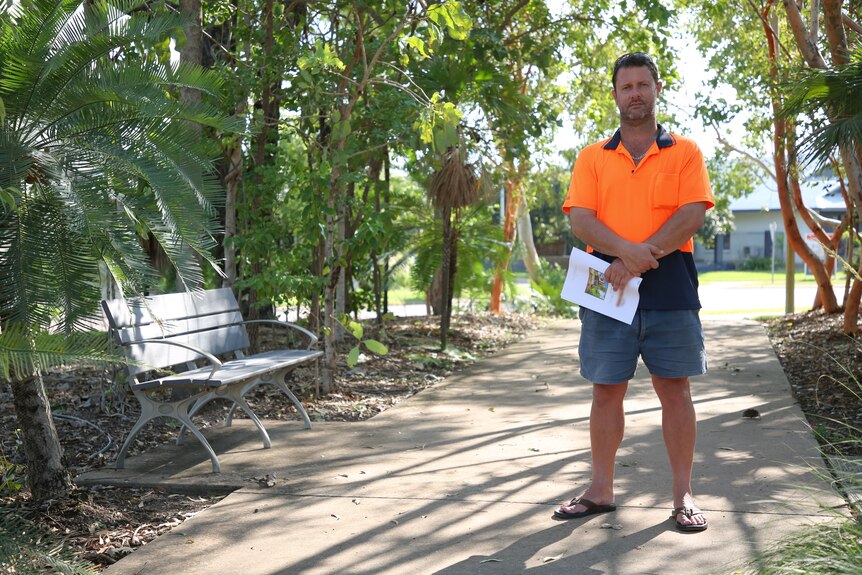 A man in a high visibility shirt standing with his arms folded, holding a report.