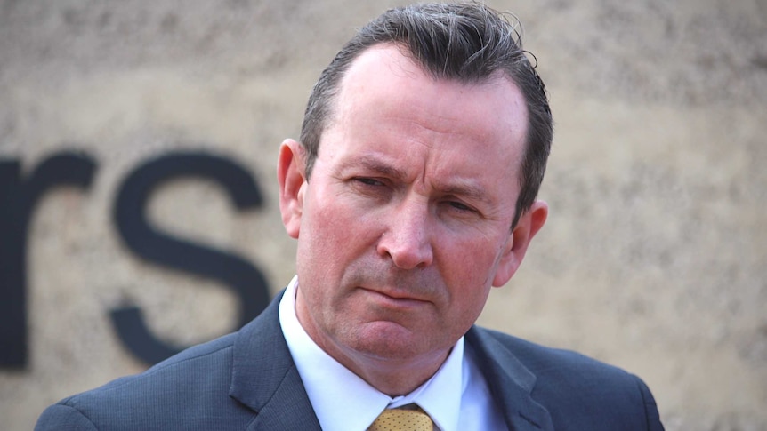 A closeup of a man in a suit and yellow tie looking stern