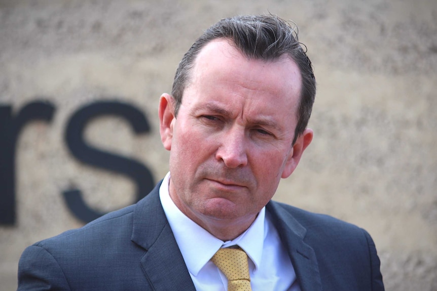 A closeup of a man in a suit and yellow tie looking stern