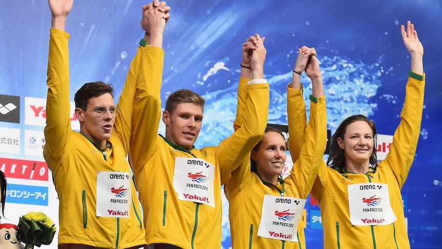 Australian swimmers raise their arms aloft on the top step of the podium
