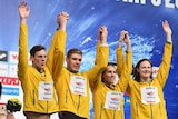 Australian swimmers raise their arms aloft on the top step of the podium