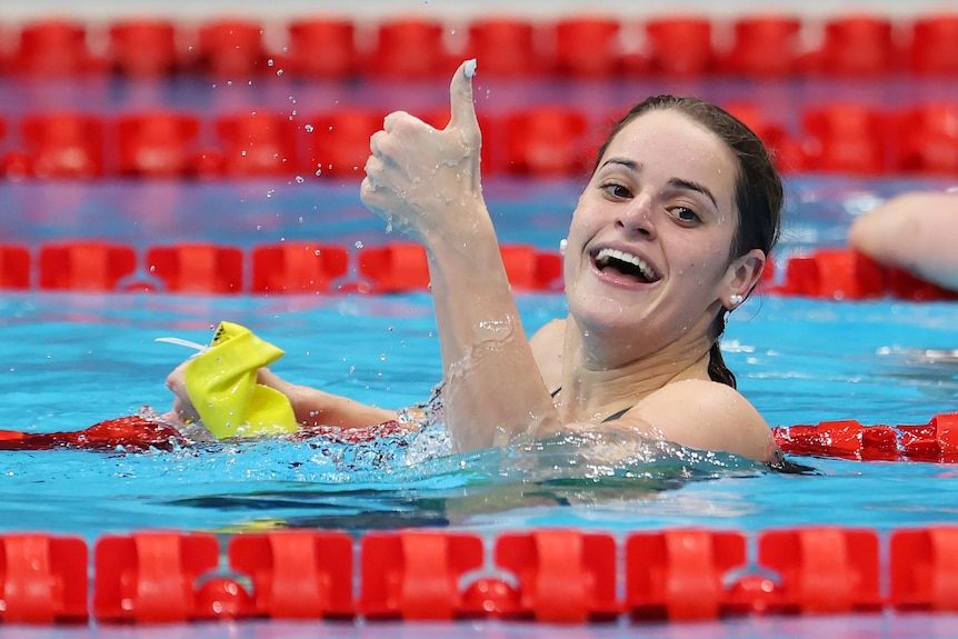 A brunette woman in a pool giving a thumbs up