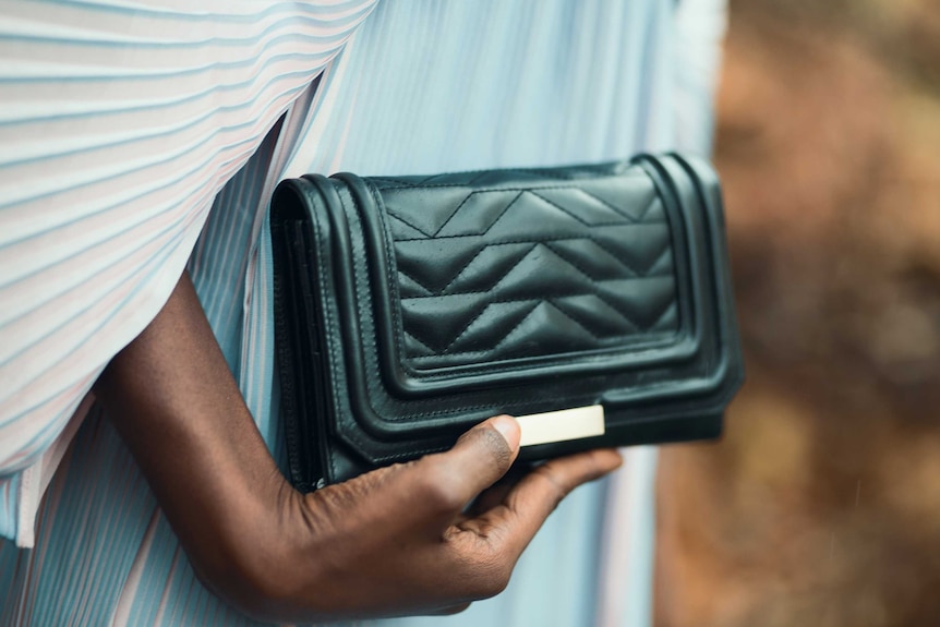 Close up of woman holding a black purse, showing that carrying cash is a good way to save your money.