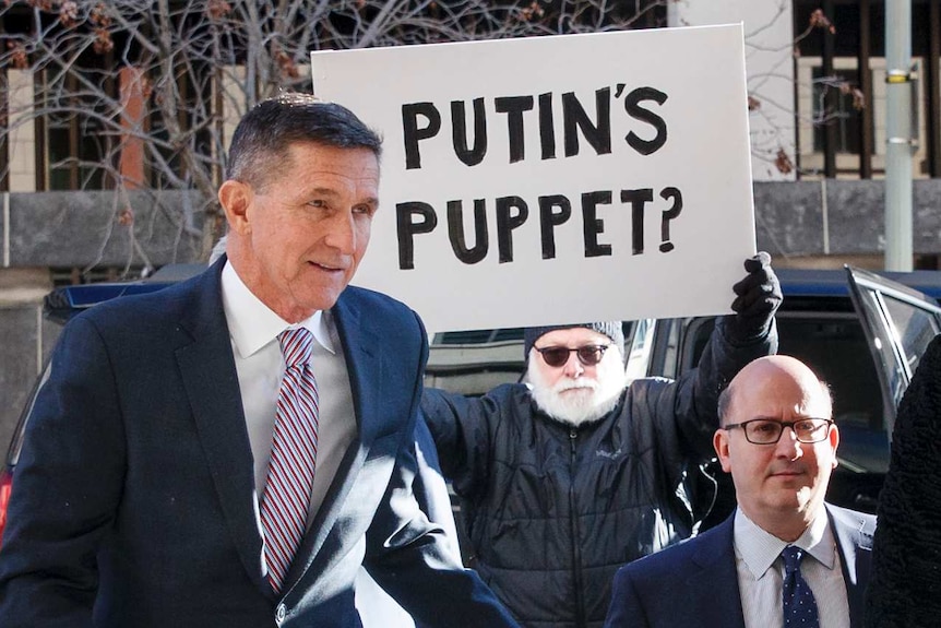 Former  National Security Advisor Michael Flynn arrives at court with protester holding sign saying Putin's Puppet