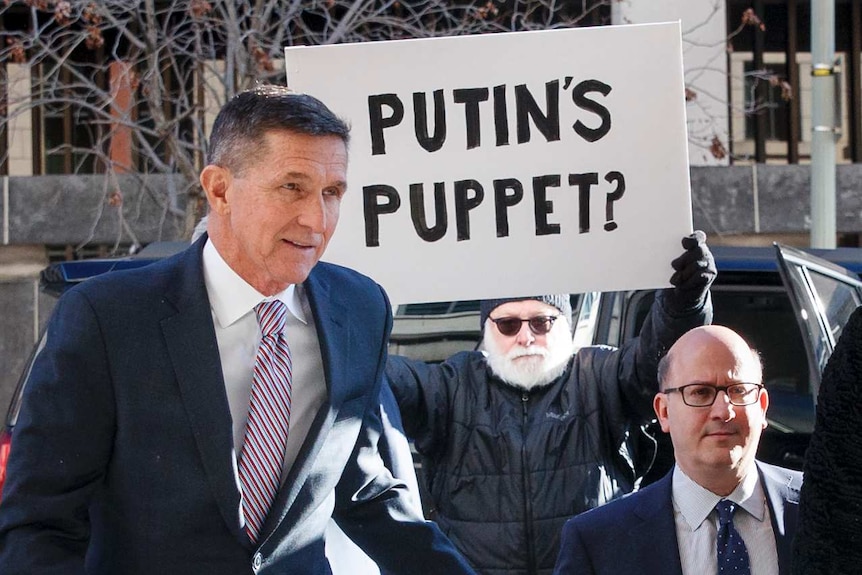 Former  National Security Advisor Michael Flynn arrives at court with protester holding sign saying Putin's Puppet?