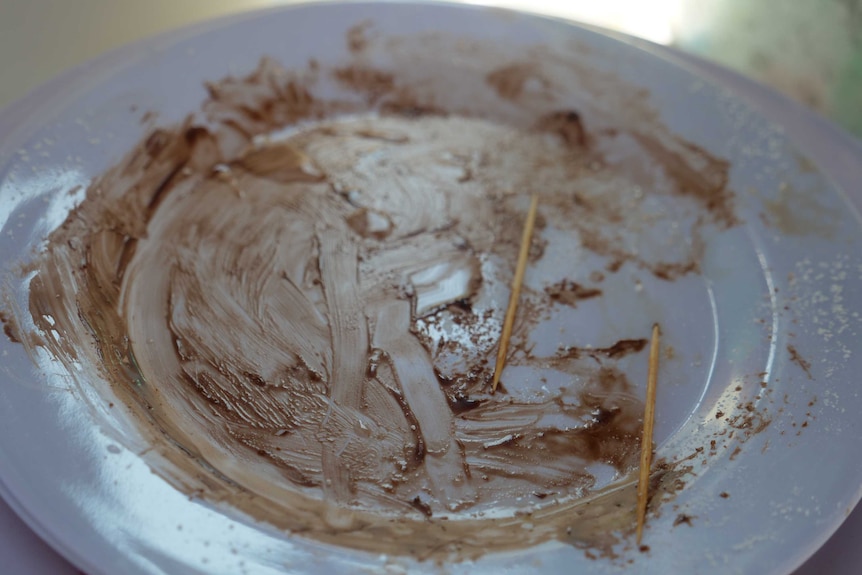 A white plate with chocolate sauce smeared over it and two toothpicks sitting on the plate.