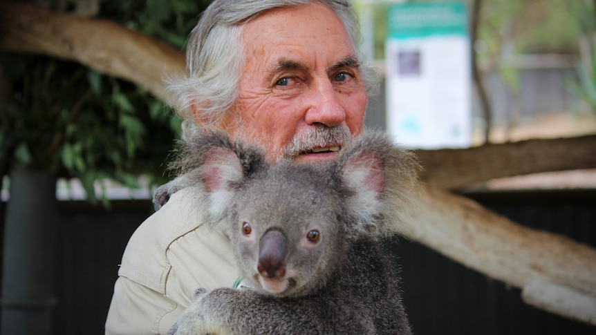 A man stares at the camera with a koala on his shoulder 