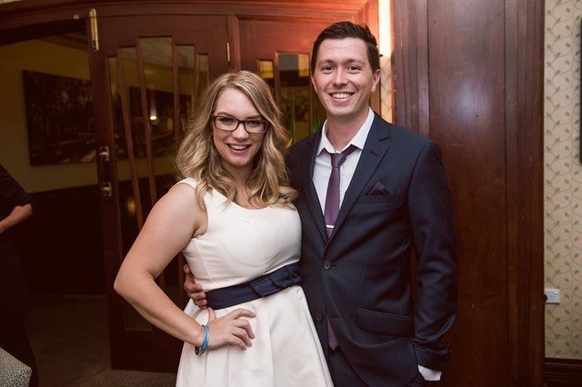 Karla Matthews wears a white dress and poses next to a man wearing a suit