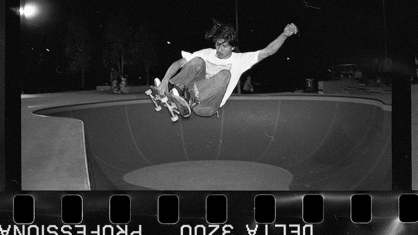 A black and white photo of a man skateboarding, with the strip of film in the foreground