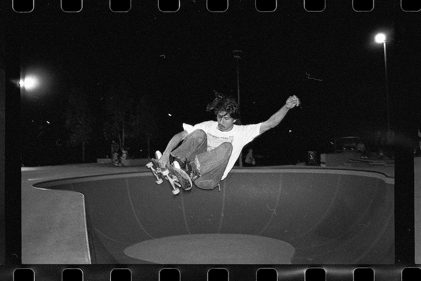 A black and white photo of a man skateboarding, with the strip of film in the foreground