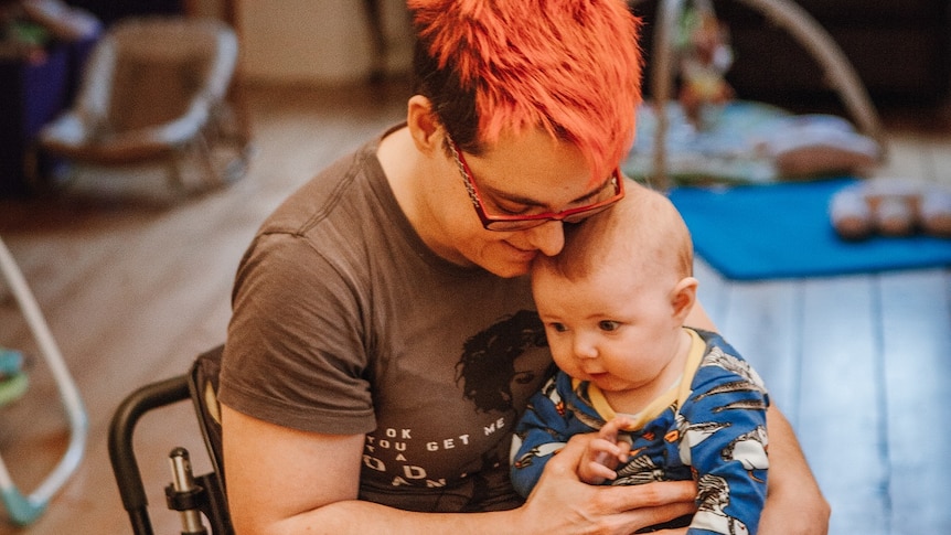 A parent with short hair and glasses holding a baby in their lap.
