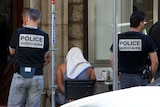 A man covered with a towel is apprehended by French police.