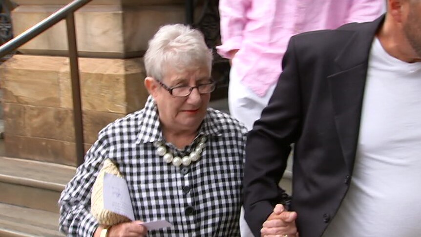 An elderly woman wearing glasses and a black and white shirt holding hands with a man