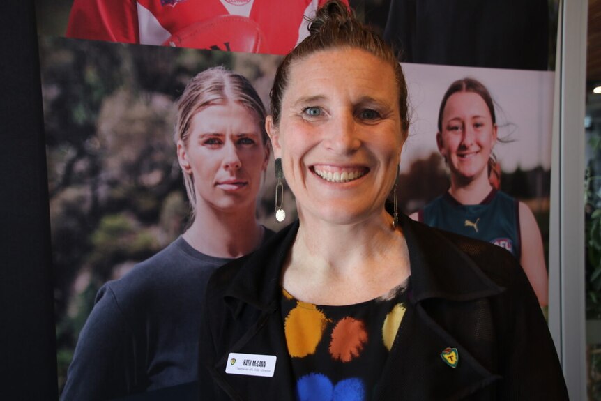 Kath is standing in front of a large poster with two footballer players on it and smiling.