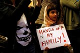 A girl holds a sign reading "Hands off my family"